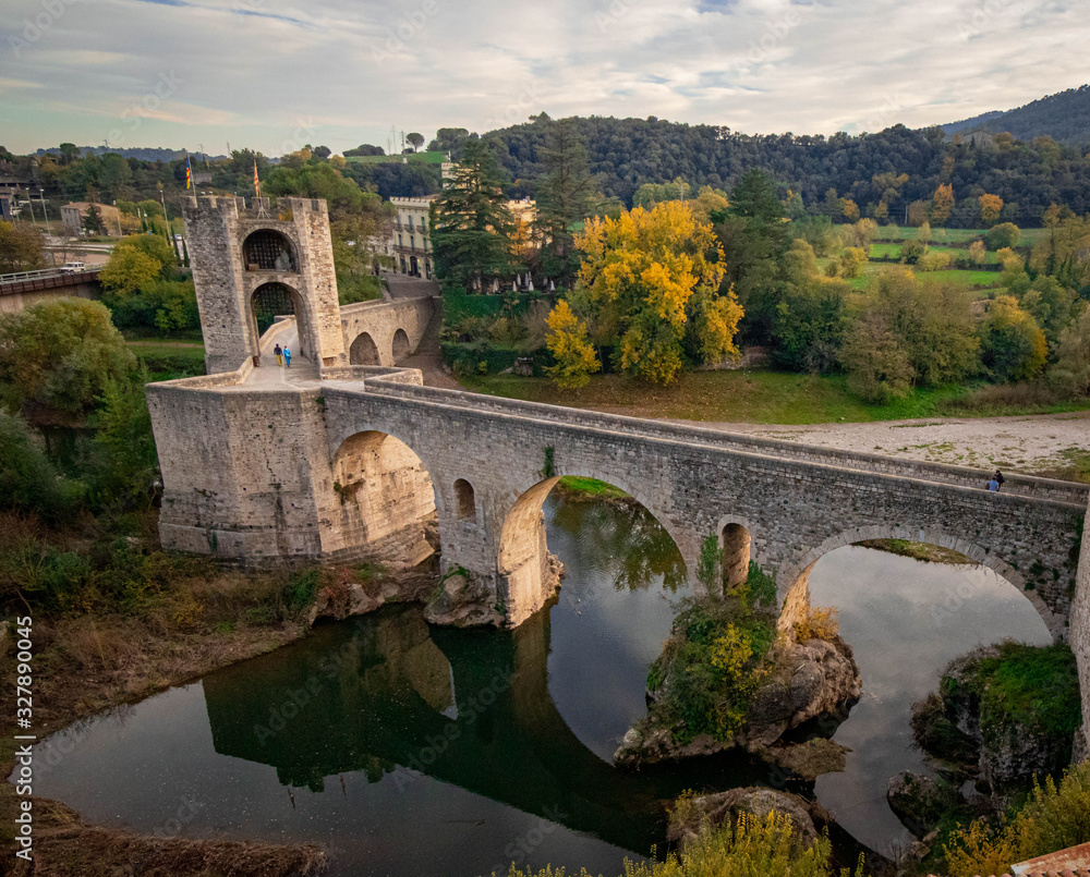 Fototapeta premium Antiguo puente sobre un rio con bosque y montañas de fondo