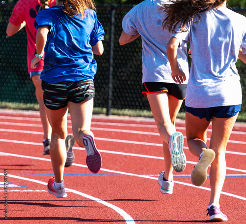 Rear view of high school girls running in a group on a track