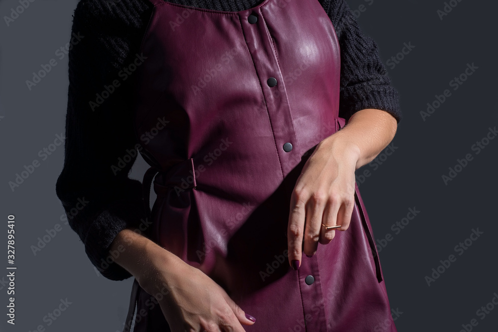 Catalog of advertising photos of a young red-haired girl in a burgundy leather sundress made of quality leather and a black sweater. On a dark gray background. Style and fashion.