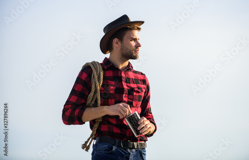 Looking for adventures. Farmer cowboy handsome man relaxing after hard working day at ranch. Lonely farmer sky background. Rustic style. Hero of western culture. Farmer drink water metal flask