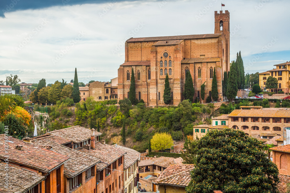 Medieval basilica di San Domenico, Siena, Tuscany, Italy. Red stone, green trees, blue sky with white clouds. Pictorial tuscan cityscape.