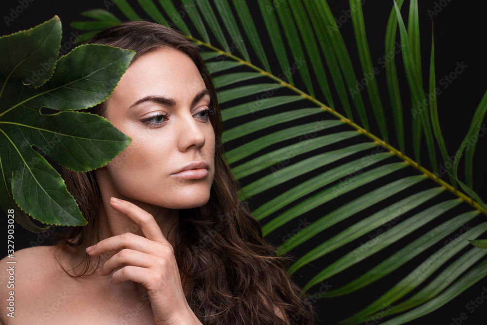 Portrait of a young beautiful woman with perfect smooth skin with a large green tropical leaf Portrait of a young beautiful woman with perfect smooth skin with a large green tropical leaf