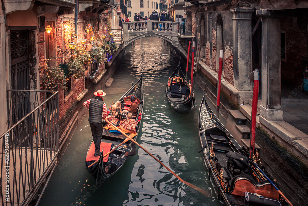 Gondolier rowing down a narrow canal in venice with christmas lights illuminating his gondola
