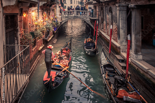 Obraz na płótnie Gondolier rowing down a narrow canal in venice with christmas lights illuminating his gondola w salonie