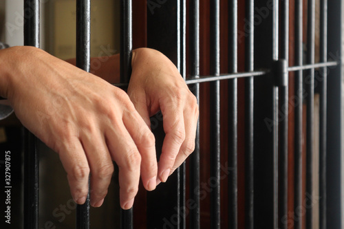 prisoner behind bars.hand of prisoner on steel jail bars.Man under arrested by policeman because illegal behaviour.
