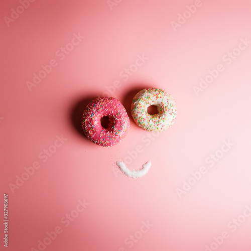 funny smiley of two donuts and sugar on a pink background with place for text, an example of junk food