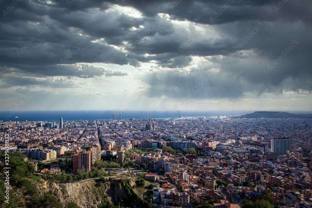 Panorama of Barcelona, Spain, viewed from the Bunkers of Carmel on a cloudy day with rays of light. Aerial top view from hill with modern buildings.