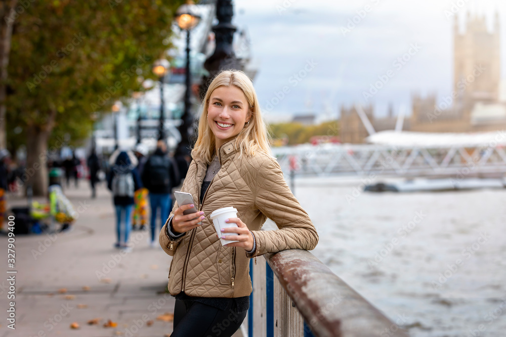 Portrait einer moderne, jungen Stadtfrau mit Handy und Kaffee in der hand am Ufer der Themse in London, Großbritannien