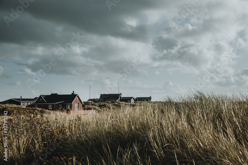 Wooden colorful weekend houses on the Rømø island in Denmark under the cloudy sky with the marram grass in the foreground during the autumn day