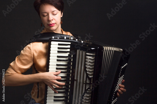 A brunette in a gold shirt, with short haircut, on a dark kground of the Studio. play the accordion