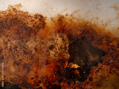 Rusty corrosion. Rusty metal surface with wet rust with smudges of water and drops. Brown, black and yellow rust and dirt on white enamel. Rusted brown and white abstract texture.