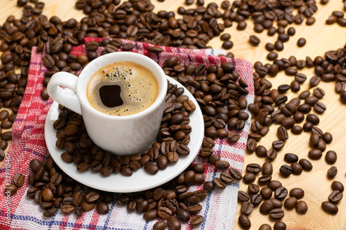 A cup of fresh coffee on napkin. A scattering of coffee beans with a cup of coffee.