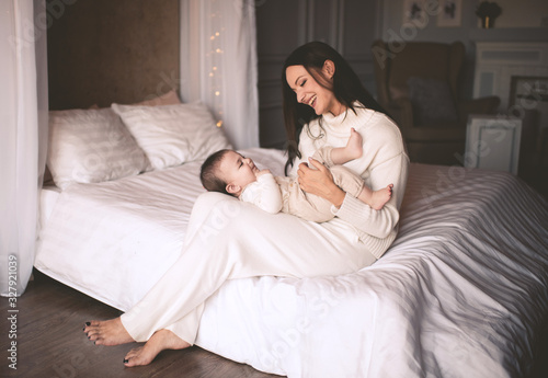 Happy woman holding baby boy in bed closeup in room. Looking at each other. Motherhood. Maternity.