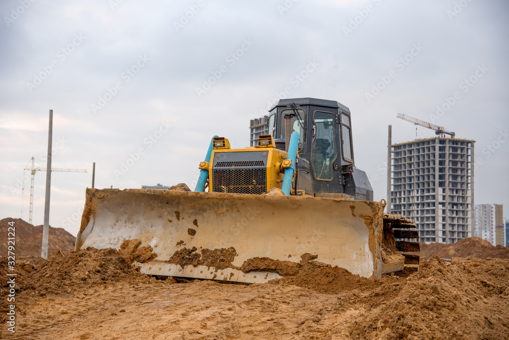 Bulldozer during land clearing and foundation digging at large construction site. Crawler tractor with bucket for pool excavation and utility trenching. Dozer, Earth-moving equipment. Bulldozer during land clearing and foundation digging at large construction site. Crawler tractor with bucket for pool excavation and utility trenching. Dozer, Earth-moving equipment.
