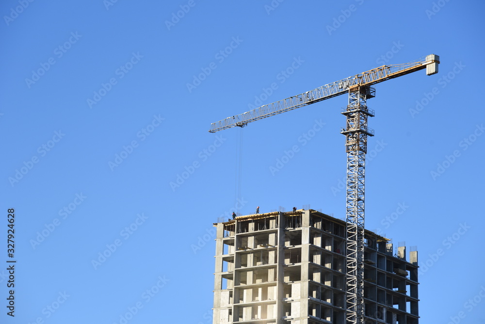 Tower cranes working at construction site against blue sky. Crane lifting a concrete bucket. Construction process of the new residential buildings. Transportation blocks and pouring of the cement mix Tower cranes working at construction site against blue sky. Crane lifting a concrete bucket. Construction process of the new residential buildings. Transportation blocks and pouring of the cement mix