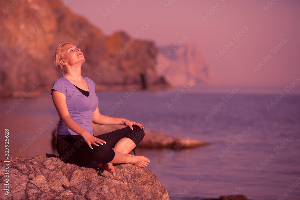 Young relaxed caucasian woman sits on a stone and enjoys the rays of the summer sun on the background of the sea during the long-awaited vacation on a summer day. Rest and recovery concept