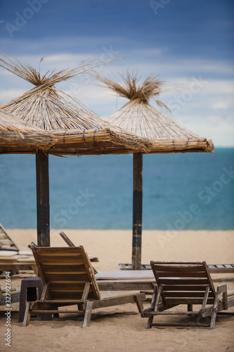 Fototapeta Naklejka Na Ścianę i Meble -  Straw beach umbrellas and wooden sun beds on a sandy beach against the sea. Beach infrastructure in Bulgaria with the inscription: 