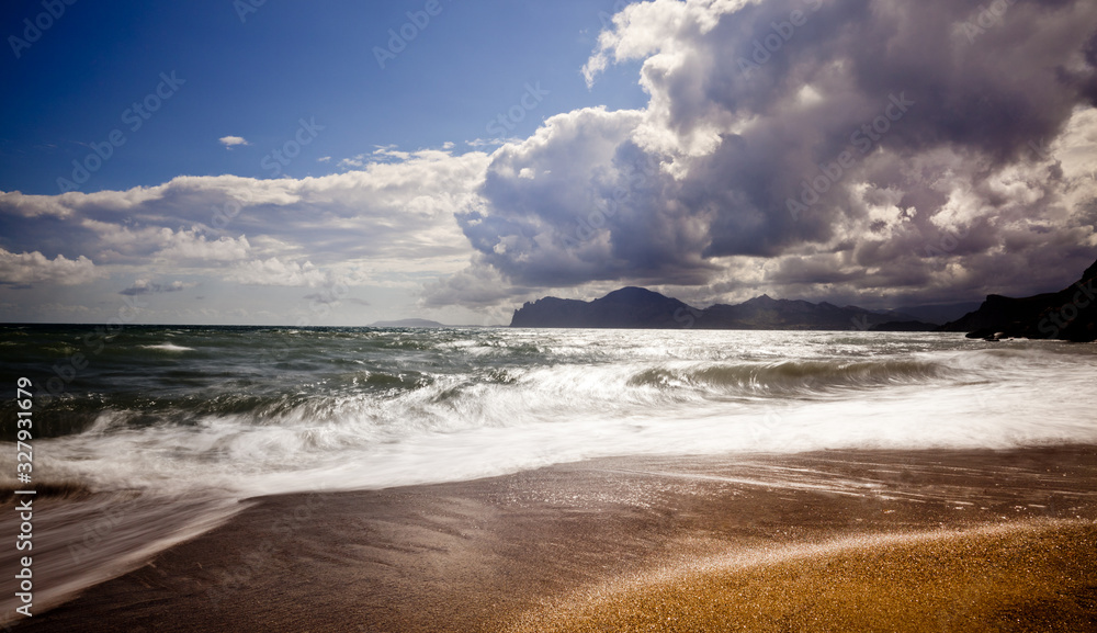 Sandy beach with mountains on background. Mountains are covered with grass, and has sheer cliffs from sea. Sky is cloudy