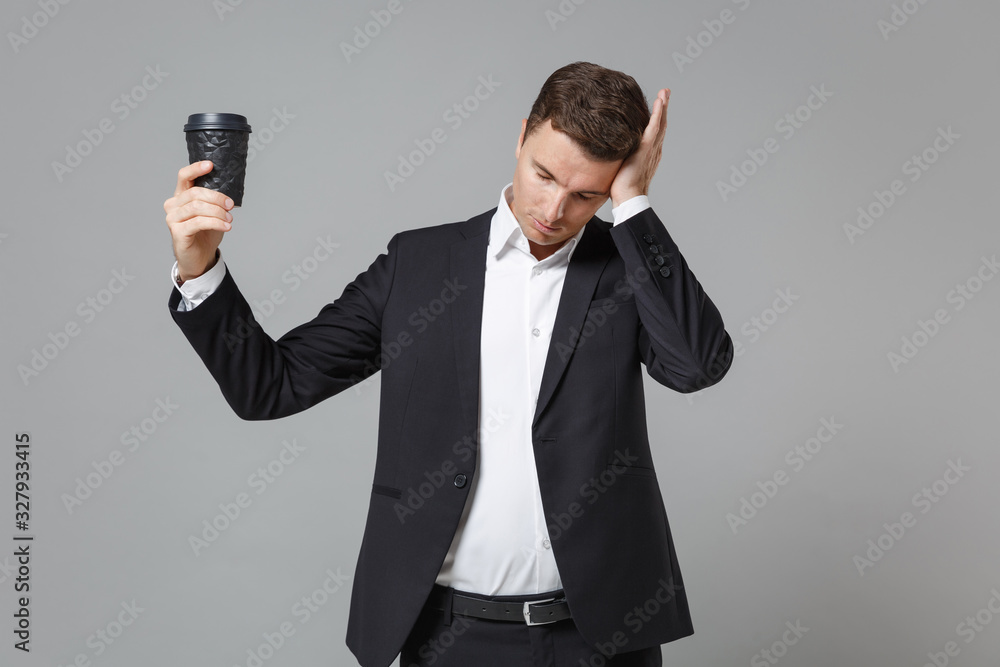 Tired young business man in classic black suit shirt posing isolated on grey background. Achievement career wealth business concept. Mock up copy space. Hold cup of coffee or tea, put hand on head. Tired young business man in classic black suit shirt posing isolated on grey background. Achievement career wealth business concept. Mock up copy space. Hold cup of coffee or tea, put hand on head.