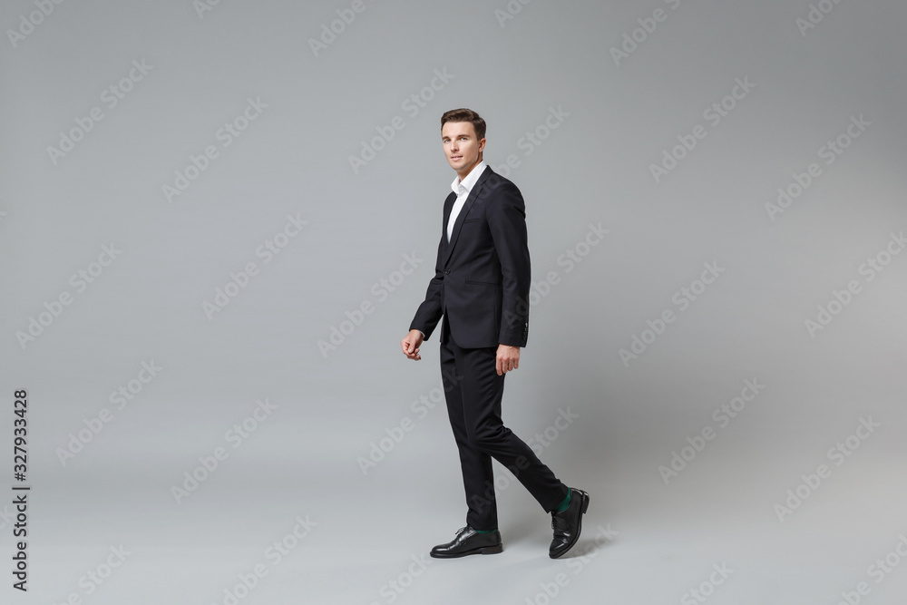Side view of confident young business man in classic black suit shirt posing isolated on grey wall background in studio. Achievement career wealth business concept. Mock up copy space. Looking camera. Side view of confident young business man in classic black suit shirt posing isolated on grey wall background in studio. Achievement career wealth business concept. Mock up copy space. Looking camera.