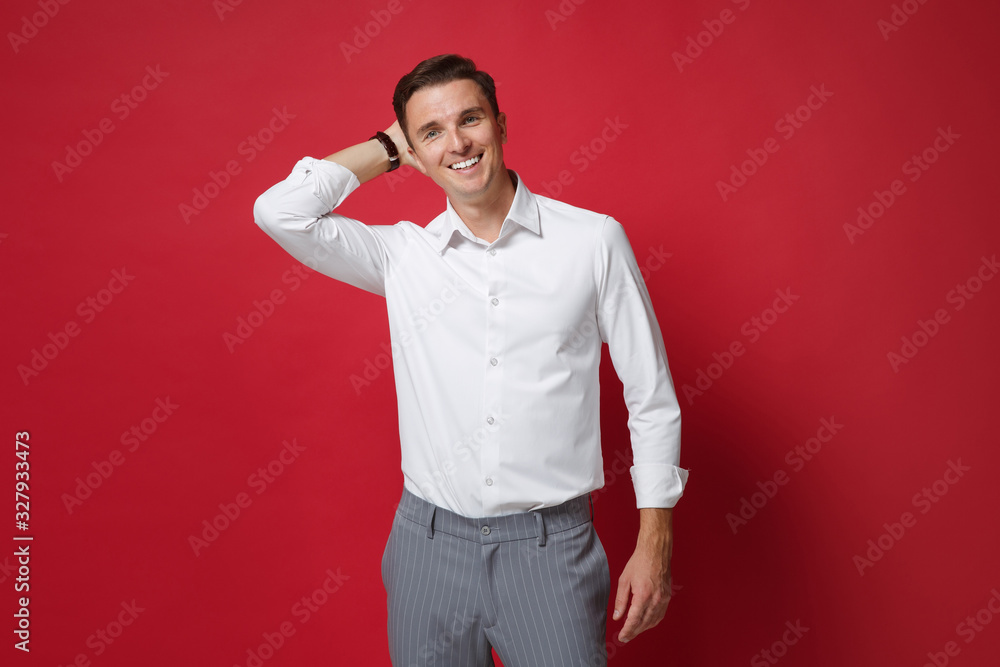 Cheerful young business man in white shirt, gray pants posing isolated on bright red wall background studio portrait. Achievement career wealth business concept. Mock up copy space. Put hand on head.