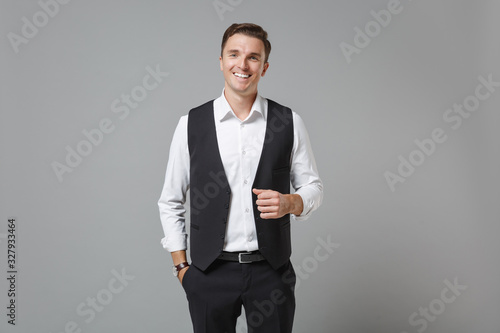 Fototapeta Smiling cheerful young business man in classic black waistcoat shirt posing isolated on grey wall background in studio