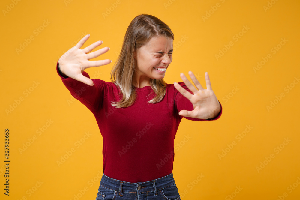 Scared young blonde woman girl in casual clothes posing isolated on yellow orange background studio portrait. People lifestyle concept. Mock up copy space. Keeping eyes closed, covering with hands.