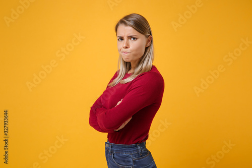 Side view of dissatisfied young blonde woman in casual clothes posing isolated on yellow orange background in studio. People lifestyle concept. Mock up copy space. Hold hands crossed, looking camera.
