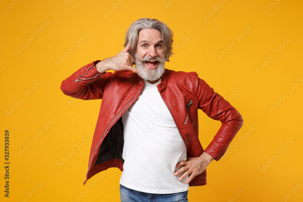 Cheerful elderly gray-haired mustache bearded man in red leather jacket posing isolated on yellow background. People lifestyle concept. Mock up copy space. Doing phone gesture like says call me back.