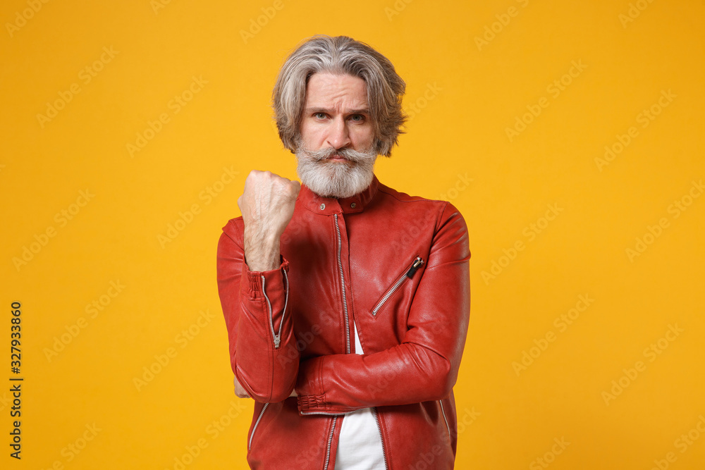 Angry concerned elderly gray-haired mustache bearded man in red leather jacket posing isolated on yellow orange wall background in studio. People lifestyle concept. Mock up copy space. Clenching fist. Angry concerned elderly gray-haired mustache bearded man in red leather jacket posing isolated on yellow orange wall background in studio. People lifestyle concept. Mock up copy space. Clenching fist.