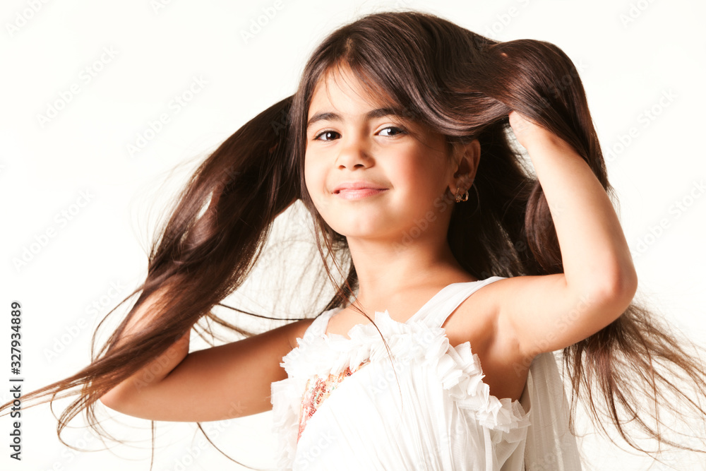 Smiling girl buried hands in her long brown hair, dressed in white blouse, isolated on white background and looking at camera Smiling girl buried hands in her long brown hair, dressed in white blouse, isolated on white background and looking at camera