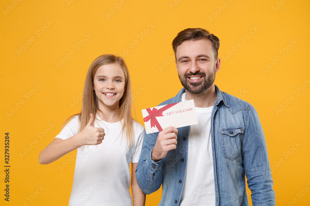 Bearded man in casual clothes with child baby girl. Father little kid daughter isolated on yellow wall background. Love family day parenthood childhood concept. Hold gift certificate showing thumb up.