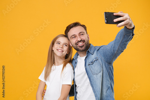 Smiling bearded man in casual clothes with child baby girl. Father little kid daughter isolated on yellow background. Love family day parenthood childhood concept. Doing selfie shot on mobile phone.