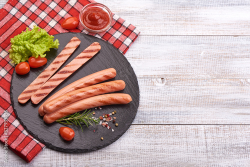 Grilled sausages with spices and herbs on a stone plate, on rustic background