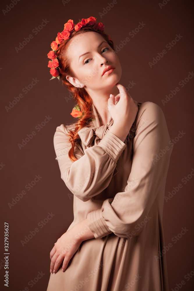Close up of attractive young lady with rose wreath on head looking aside. Charming girl wearing elegant decoration in hair. Isolated on brown studio background. Concept of beauty and elegance.