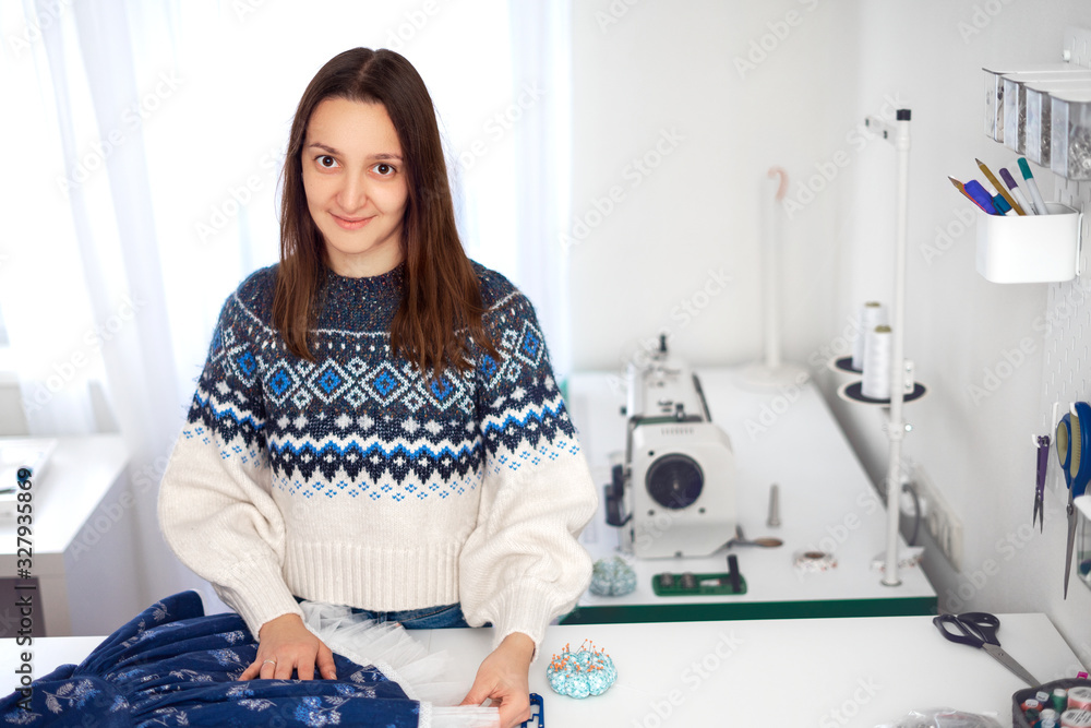 Young seamstress sewing dress. Seamstress workplace with tailor s accessories and sewing machine in studio. Seamstress checks the finished dress. Copy space Young seamstress sewing dress. Seamstress workplace with tailor s accessories and sewing machine in studio. Seamstress checks the finished dress. Copy space