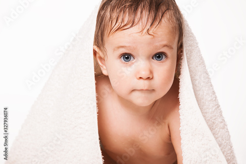 Close up of adorable child with wet hair looking at camera with wide opened eyes. Sweet infant with white soft towel on head. Isolated on white studio background. Concept of baby hygiene.