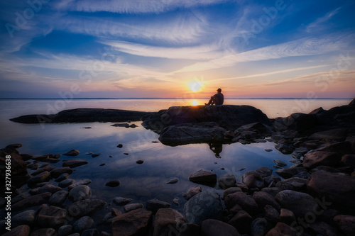 Man sitting on a cliff by a lake during sunset