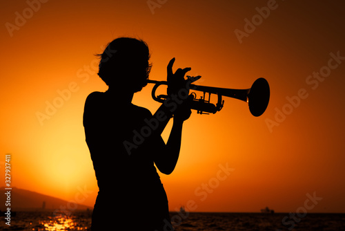 Silhouette of a Young woman plays trumpet on sunset. © ardasavasciogullari