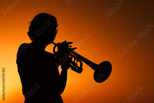 Silhouette of a Young woman plays trumpet on sunset.