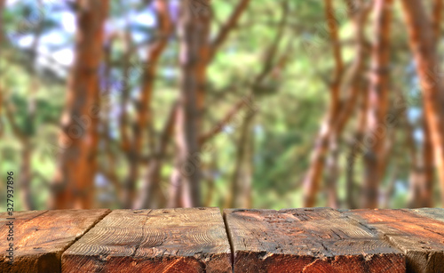 Weathered empty wooden table in front on a pine forest background. Table in perspective view with copy space for producs and objects mockup. Aged wood.