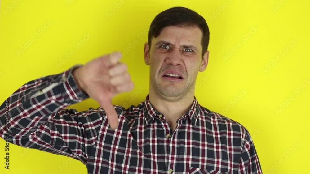 Funny handsome guy shows thumb down expressing his disapproval. Portrait of a young guy, he shows thumb down expressing disagreement. Portrait on a yellow background. Funny handsome guy shows thumb down expressing his disapproval. Portrait of a young guy, he shows thumb down expressing disagreement. Portrait on a yellow background.