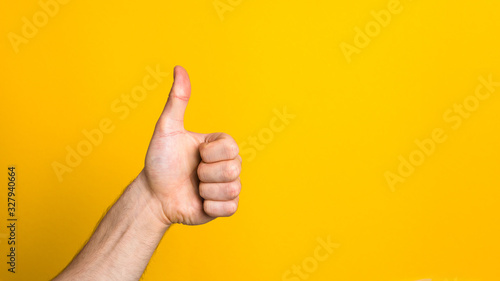 checked and approved. man hand showing big thumb up like sign against yellow background with copyspace for advert photo