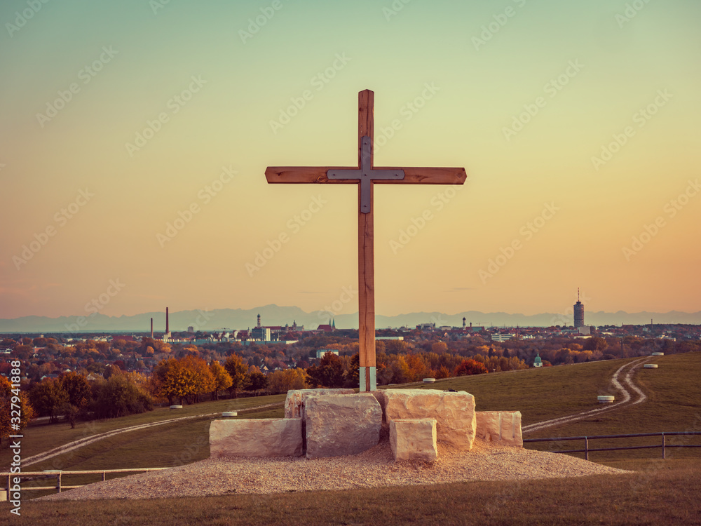 Panorama image of Augsburg skyline during sunset with mountains in the background and wooden cross in the front