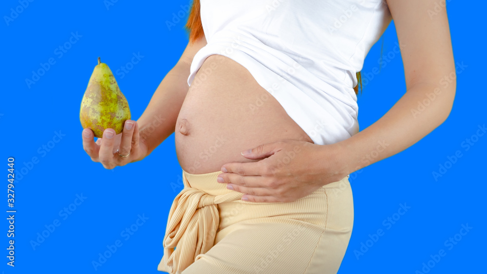 A happy pregnant young woman holding a pear next to her belly showing