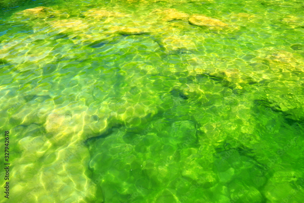 Yellow stones lie in the clear clear green water in the mountain river Krka in Croatia. Natural water background in lake or river, ecology