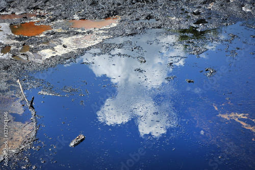 Spills of crude oil on the soil surface - environment pollution. Cloudy sky reflected in a puddle of oil