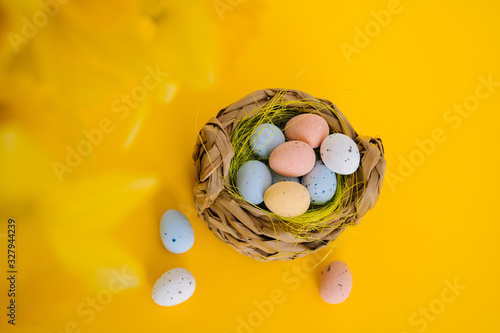 Easter holiday decorations on yellow background. Colored painting speckled eggs in basket. Creative spring composition with Easter elements - flowers and eggs. Celebrating Easter concept at spring.