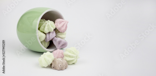 Marshmallow multicolored. Meringue marshmallows in a green cup on a light background. Colorful meringues on a white background. Lots of sweet marshmallows. Marshmallow drops from a cup. Banner. copysp