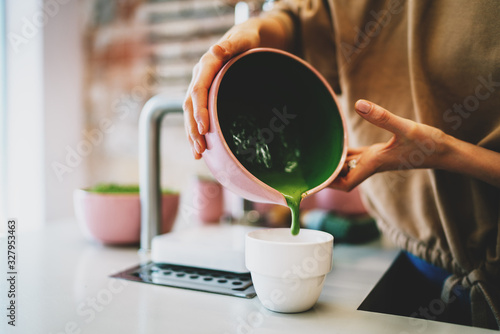 Fototapeta Super natural matcha tea made by professional barista in a coffee shop. Woman's hands holding a bowl with a matcha tea ready to be poured to the cup and served. Tea ceremony in a oriental style.